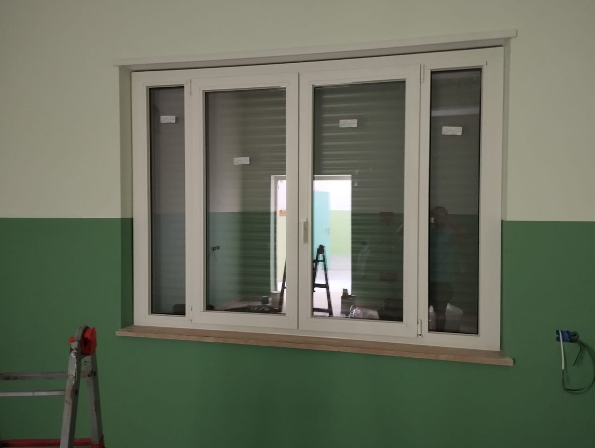 Finestra bianca in PVC a quattro ante con etichette sui vetri e davanzale in marmo su parete verde, scala in cantiere